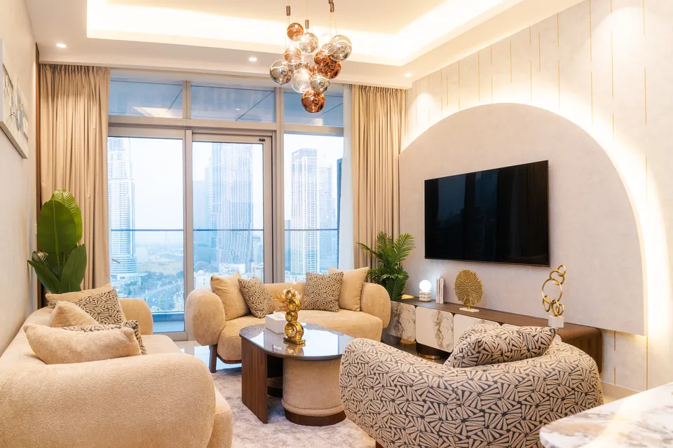 Imperial Avenue Apartment, Downtown Dubai: living room with a lit arch behind the TV, cream sofas and city views.